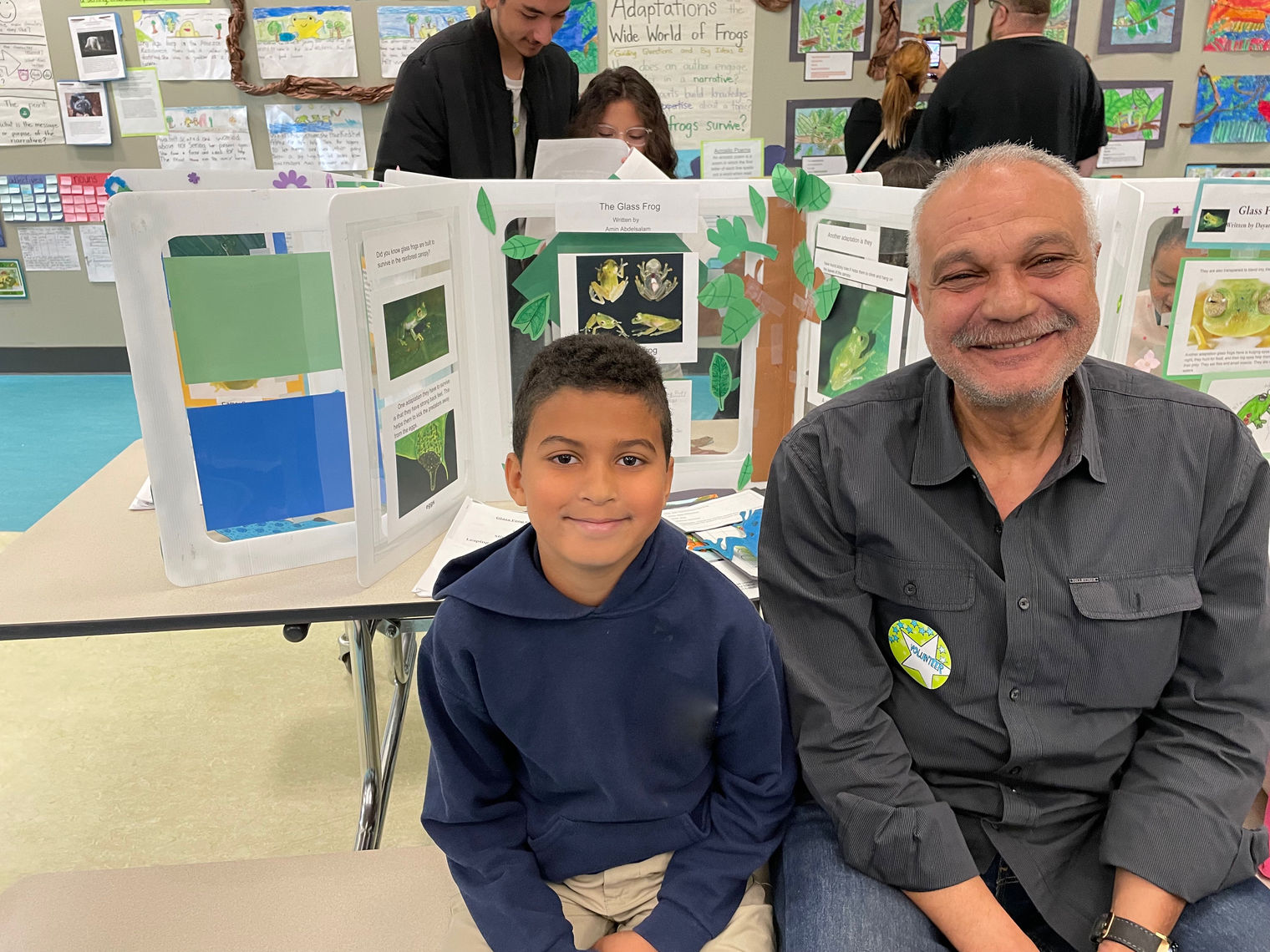 boy sits with his grandfather in front of a school display about frogs