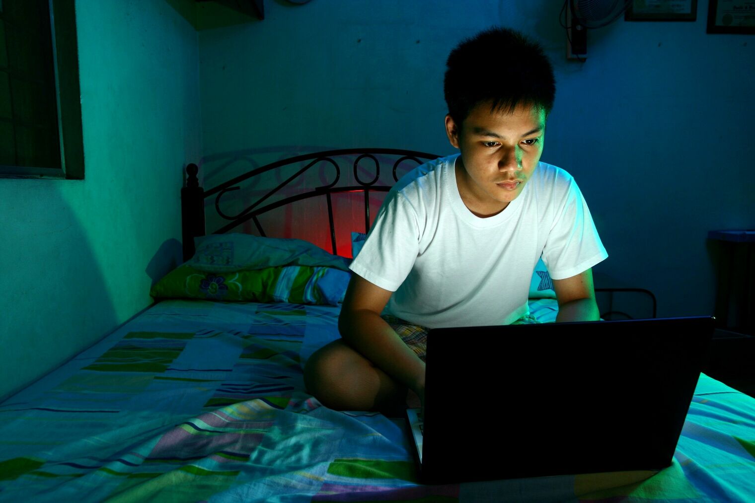 teen boy on bed using a laptop in dark room