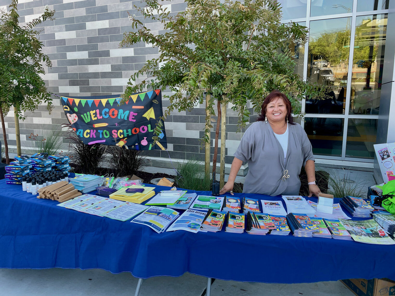 a woman smiles while standing at a table filled with helpful items for families. Sign behind her says Welcome back to School