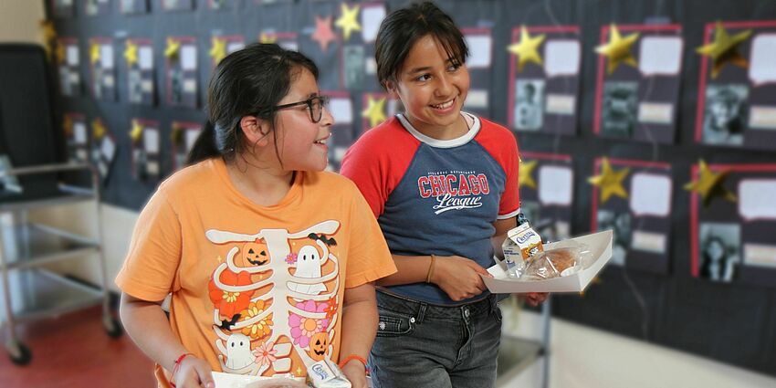 two smiling girls walking with their lunch trays