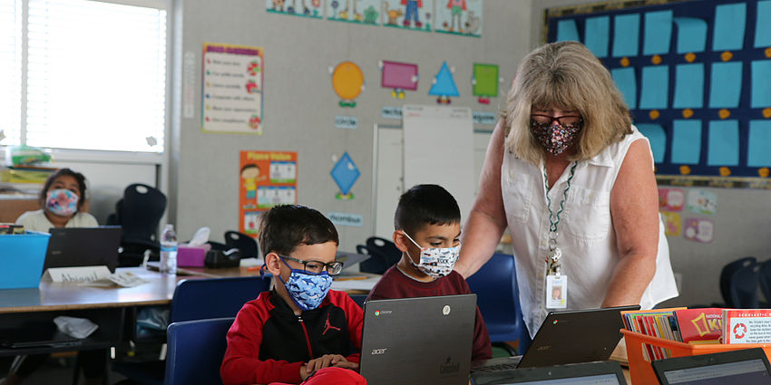 teachers assists students. All wearing masks.