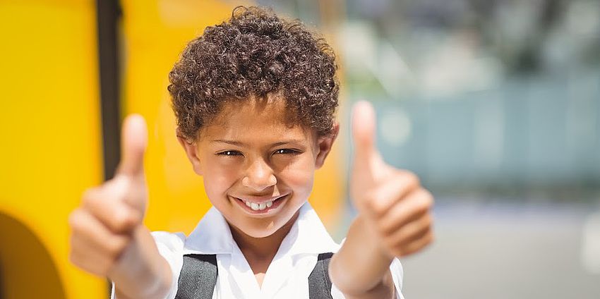 Student putting both thumbs up in front of school bus.