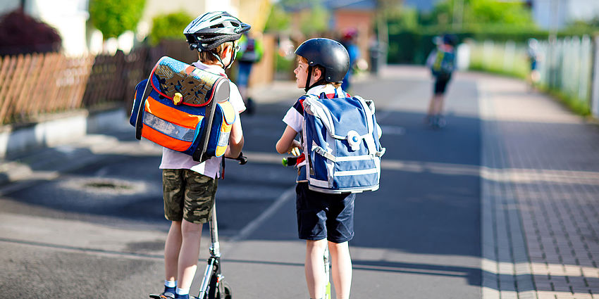 two boys with backpacks on scooters