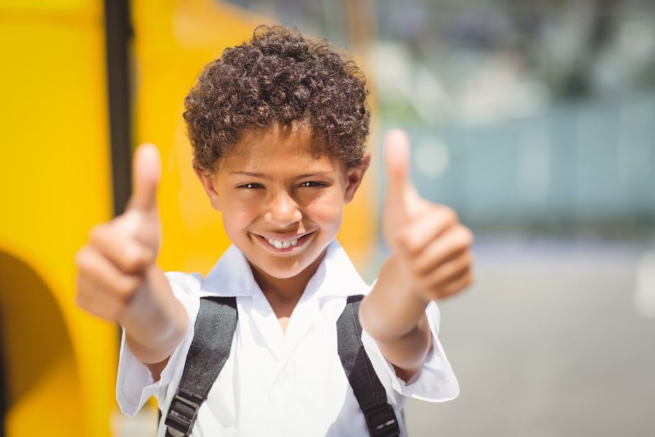 Student putting both thumbs up in front of school bus.