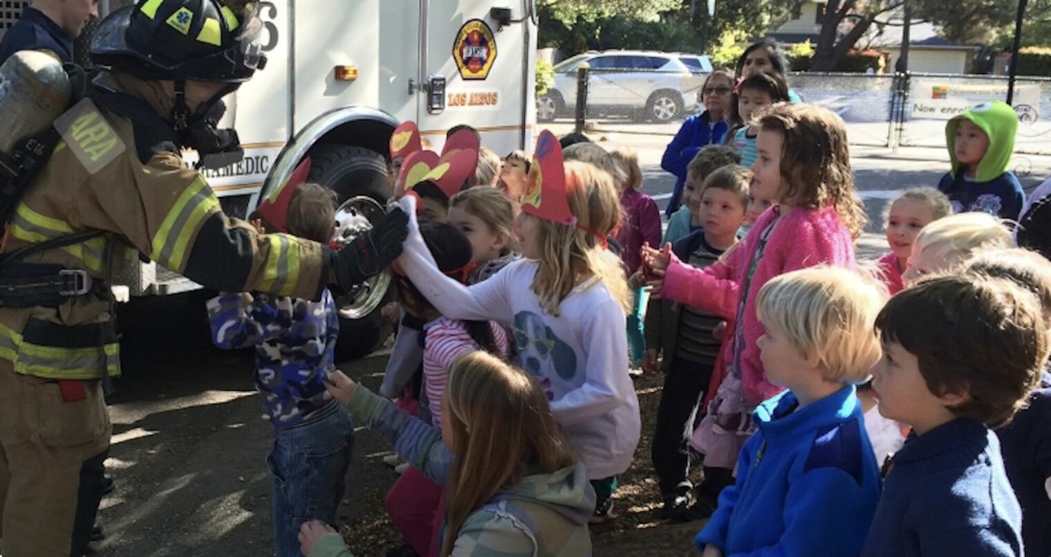 children gather around a firefighter as he shows them the fire truck